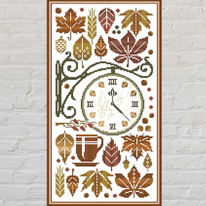 Puede incluir: Diseño de punto de cruz que muestra un reloj, hojas y una taza de café. El reloj tiene números romanos y está rodeado de hojas de otoño en tonos marrón, dorado y verde. También se incluye una taza de café y un platillo.