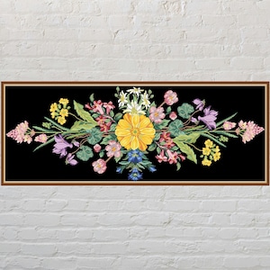 May include: A framed floral embroidery on a black background. The embroidery features a large yellow flower at the center, surrounded by pink, purple, and white flowers, with green leaves. The frame is brown.