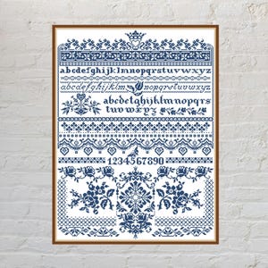May include: A cross-stitch sampler featuring dark blue thread on a white background. The design includes three distinct alphabet rows, a row of numbers from 1 to 0, decorative floral borders, heart motifs, and a crown icon at the top center.
