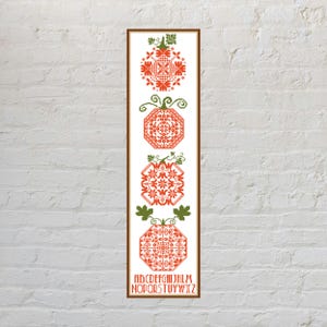 May include: A vertical rectangular cross-stitch pattern featuring four orange pumpkins with green stems and leaves, each decorated with intricate geometric and floral motifs. Below the pumpkins, the alphabet is stitched in orange capital letters.