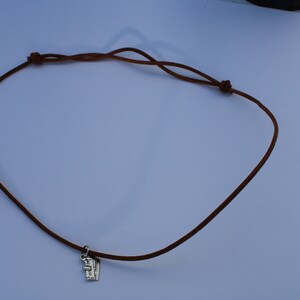 Może przedstawiać: Brązowy sk&oacute;rzany naszyjnik z srebrnym zawieszką.