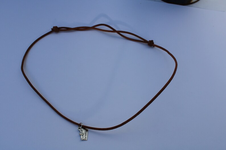 Może przedstawiać: Brązowy sk&oacute;rzany naszyjnik z srebrnym zawieszką.