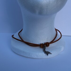 Może przedstawiać: Brązowy sk&oacute;rzany naszyjnik ze srebrnym wisiorkiem w kształcie ptaka.