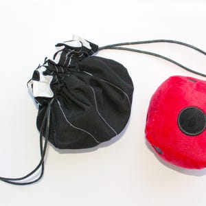 May include: A black and white striped fabric bag with a drawstring closure, and a red plush dice with a black circle in the center.