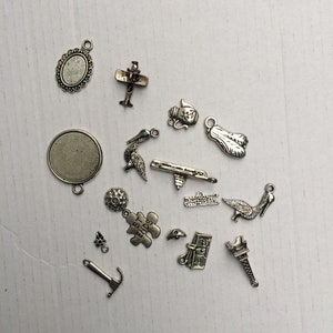 Może przedstawiać: Kolekcja srebrnych metalowych zawieszek, w tym samolot, czajnik, ptak, element układanki, piłka golfowa, młotek, książka, wieża Eiffla i kilka innych abstrakcyjnych kształt&oacute;w.