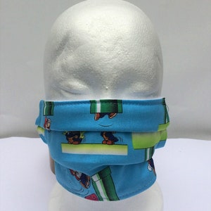 May include: A blue face mask with a repeating pattern of a video game character running through a green pipe. The character is wearing a red hat and overalls.