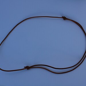 Może przedstawiać: Brązowy sk&oacute;rzany sznurek do naszyjnika z dwoma węzłami na końcach.