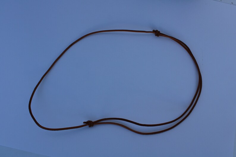 Może przedstawiać: Brązowy sk&oacute;rzany sznurek do naszyjnika z dwoma węzłami na końcach.