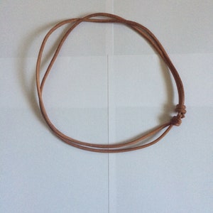 Może przedstawiać: Prosty naszyjnik ze sk&oacute;rzanego sznurka w kolorze brązowym z zawiązaną klamrą.