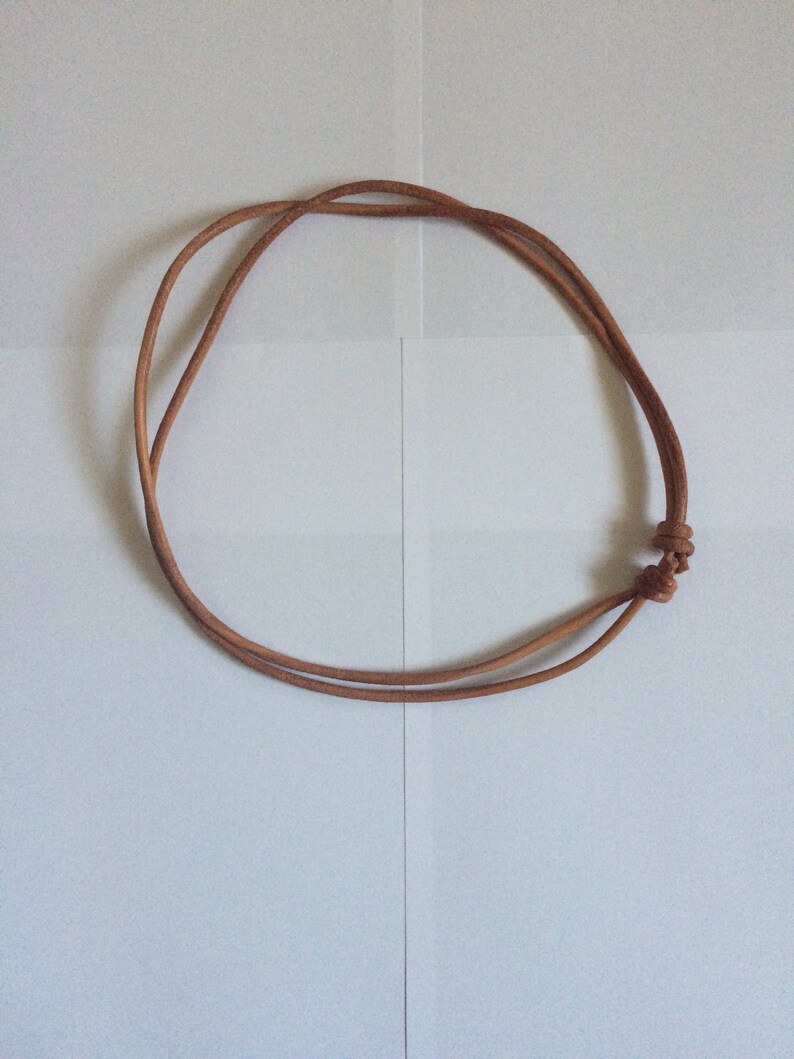 Może przedstawiać: Prosty naszyjnik ze sk&oacute;rzanego sznurka w kolorze brązowym z zawiązaną klamrą.
