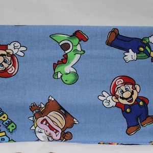 May include: Blue fabric with a repeating pattern of Mario, Luigi, Yoshi, and Bowser characters from the Super Mario Bros. video game. The fabric has the words "Super World" printed on it.