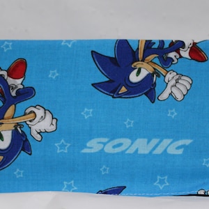 May include: Blue fabric wallet featuring a Sonic the Hedgehog design. The wallet has a blue background with white stars and two images of Sonic running. The text "SONIC" is printed in white on the fabric.