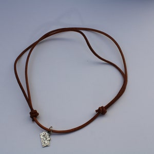 Może przedstawiać: Brązowy sk&oacute;rzany naszyjnik z zawieszką z napisem "LOVE" wykonaną ze srebra.