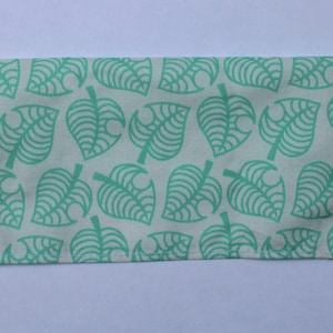 May include: A white fabric pouch with a green leaf pattern. The pouch is sewn with a white thread.