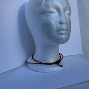 Może przedstawiać: Brązowy sk&oacute;rzany naszyjnik z wisiorem w kształcie srebrnej strzały.