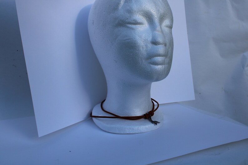 Może przedstawiać: Brązowy sk&oacute;rzany naszyjnik z wisiorem w kształcie srebrnej strzały.