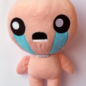 May include: A pink plush toy with a sad face, black eyes, and blue teardrop markings. The toy has a white name tag that reads "ISAAC".