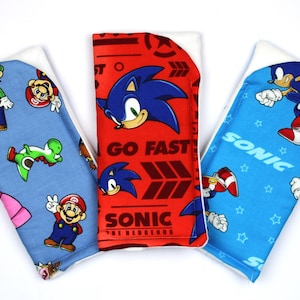 Könnte beinhalten: Drei bunte Baby-Spucktücher. Eines ist blau mit Mario-, Luigi- und Yoshi-Figuren. Das zweite ist rot mit Sonic the Hedgehog und dem Text "GO FAST". Das dritte ist blau mit Sonic the Hedgehog und dem Text "SONIC".