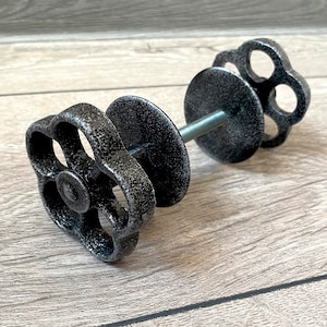 May include: A dumbbell-shaped decorative object with a threaded rod and two black, flower-shaped handles. The handles and central discs have a textured, metallic finish. The object is designed to resemble a vintage valve handle.