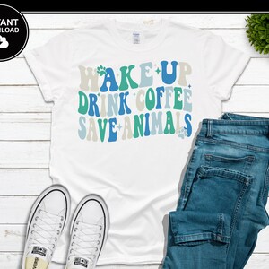 May include: White t-shirt with the text "WAKE UP DRINK COFFEE SAVE ANIMALS" in blue, green, and gray lettering. The shirt is paired with blue jeans and white Converse sneakers. A black circle with the words "INSTANT DOWNLOAD" is in the upper left corner.