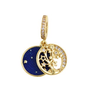 May include: A gold-coloured charm pendant featuring a blue enamel disc with stars and a circular design with a tree and stars. The tree and stars are embellished with small, clear crystals. The pendant has a small, crystal-studded loop.