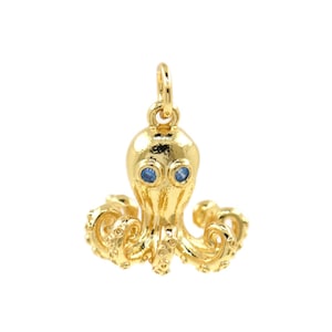 May include: A gold-colored octopus charm with blue gemstone eyes. The charm has detailed tentacles and a loop for attaching to a necklace or bracelet. The octopus is a marine-themed jewelry item.