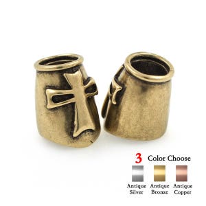 May include: Two antique bronze-colored metal beads with a cross design. The beads have a cylindrical shape with a cross on the front. The image also shows color options: antique silver, antique bronze, and antique copper.