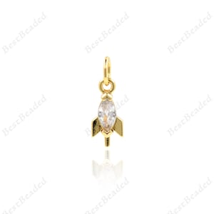 Puede incluir: Un dije de oro con un cristal transparente de forma marquesa engastado en un diseño de cohete.