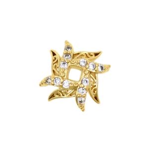 May include: A gold-colored, star-shaped jewelry piece with a square center. The piece features clear, round gemstones and ornate, swirling filigree details. The design is symmetrical and set against a white background.