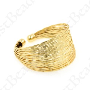 Può includere: Un anello dorato con una fascia larga realizzata con più fili sottili e intrecciati. L'anello è aperto e regolabile.