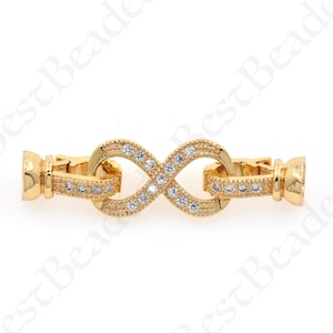 May include: Gold infinity charm with clear crystal accents. The charm has a clasp on each end for attaching to a bracelet or necklace.
