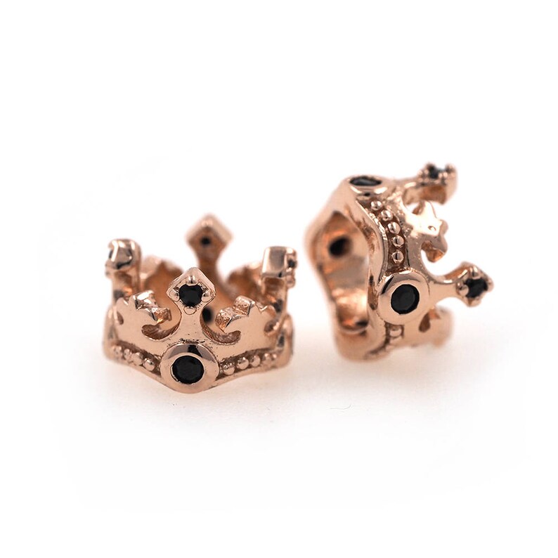 May include: Two gold-toned crown-shaped beads with black gemstones. The beads are designed to be used in jewelry making.