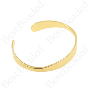 May include: A gold-colored metal bangle bracelet with a smooth, rounded surface.