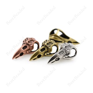 May include: Three metal bird skull beads in different colors: copper, brass, and silver. The beads are detailed and have a realistic bird skull design.