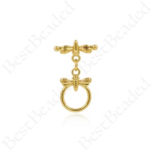 Op de afbeelding: Goudkleurige libel charm met een ring eraan bevestigd. De libel heeft ingewikkelde details en hangt aan een ketting.