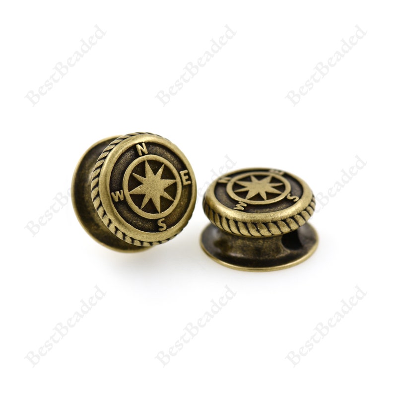 May include: Two antique gold-toned metal compass charm beads with a rope design around the edge. The compass features a star with the letters N, E, S, and W around the star.