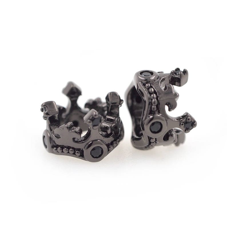 May include: Two black metal crown-shaped beads with black gemstones. The beads are designed to be used for jewelry making.