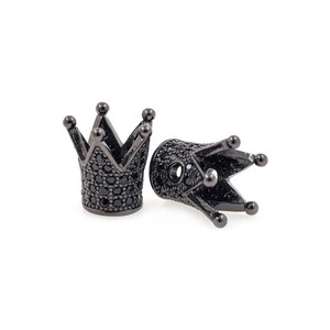 May include: Two black metal crown-shaped bead caps with black cubic zirconia stones. The bead caps are designed to be used as end caps for necklaces or bracelets.