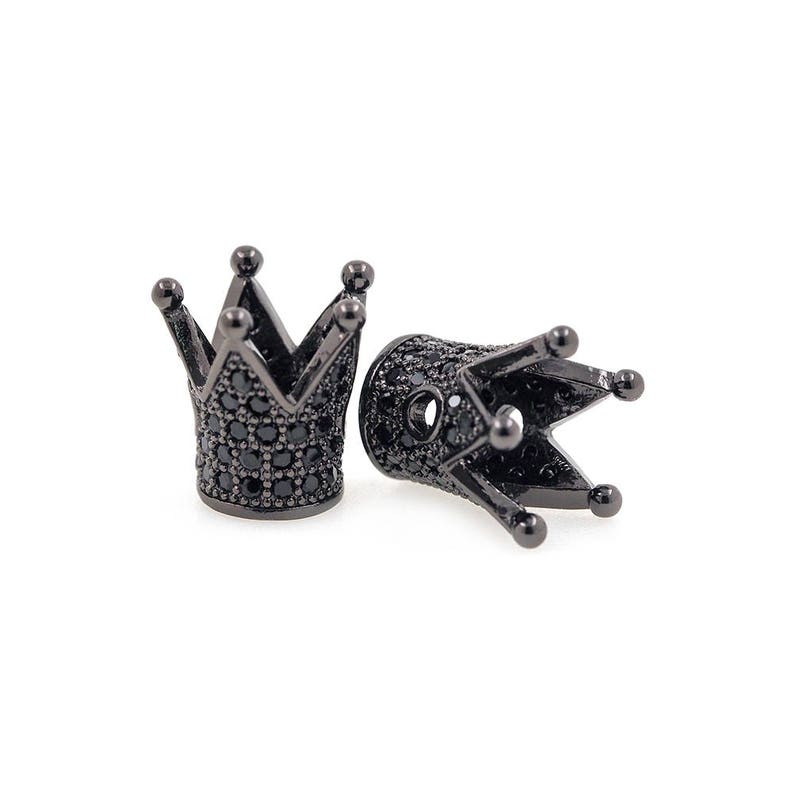 May include: Two black metal crown-shaped bead caps with black cubic zirconia stones. The bead caps are designed to be used as end caps for necklaces or bracelets.