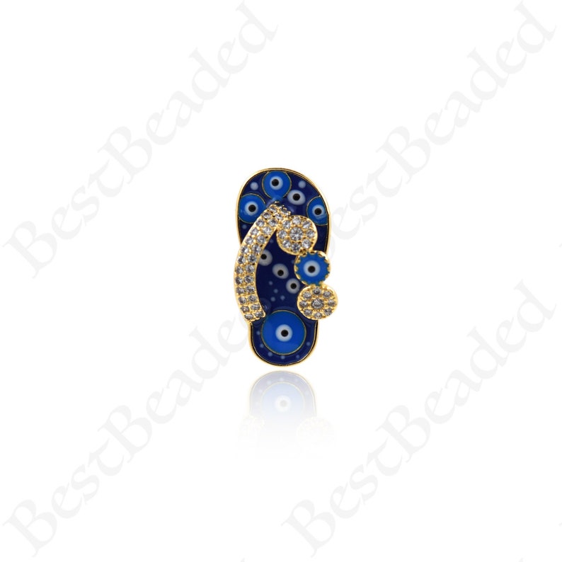 May include: Gold charm in the shape of a blue flip-flop with white and blue evil eye details. The charm is decorated with clear rhinestones.