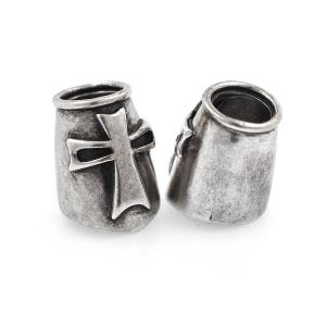 May include: Two silver-toned metal beads with a cross design. The beads have a cylindrical shape with a slightly flared top. The cross is prominently displayed on the front of each bead, adding a religious or symbolic element.