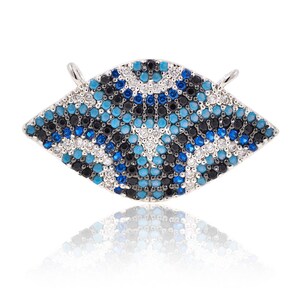 May include: A silver charm with a blue, black, and white geometric pattern. The charm is shaped like an eye and is covered in small, sparkling stones.