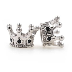 May include: Two silver crown-shaped beads with black gemstones. The beads are detailed with intricate designs and have a smooth, polished finish.