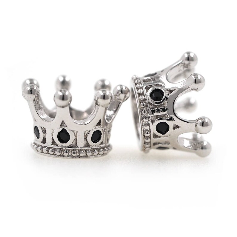 May include: Two silver crown-shaped beads with black gemstones. The beads are detailed with intricate designs and have a smooth, polished finish.