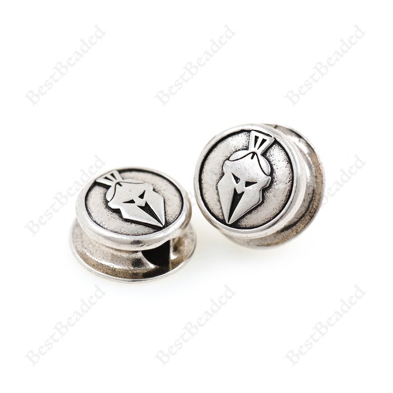 May include: Two silver-toned metal beads with a raised design of a Spartan helmet. The beads have a hole in the center for threading.