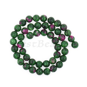 Peut inclure: Un brin de perles de pierres précieuses vertes et roses. Les perles sont rondes et ont un aspect moucheté.