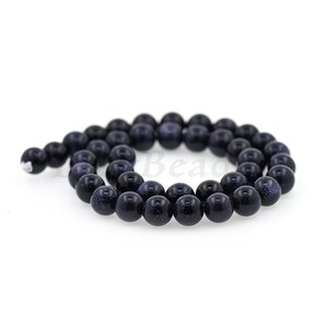 May include: A strand of dark blue round beads with a speckled texture. The beads are made of natural stone and have a polished finish.