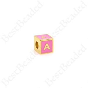K&ouml;nnte beinhalten: Goldfarbener Alphabet-Perle mit pinkfarbener Emaille-Beschichtung und dem Buchstaben "A" in Gold.