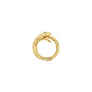 May include: A gold-colored ring in the shape of a snake eating its tail, with a textured surface. The snake's head has a small, light-colored stone for an eye. The ring is a circular shape with a clasp.