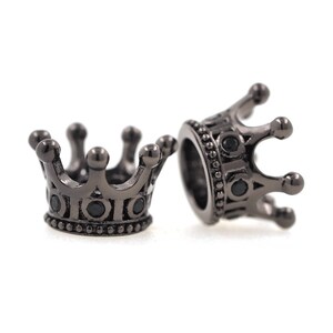 May include: Two black metal crown-shaped beads with black gemstones. The beads are designed to be used for jewelry making.